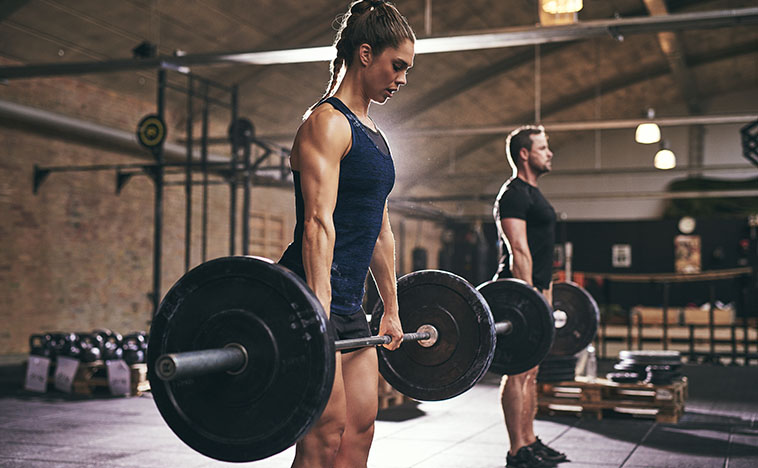 Strong woman and man holding heavy barbells in gym. Horizontal indoors shot