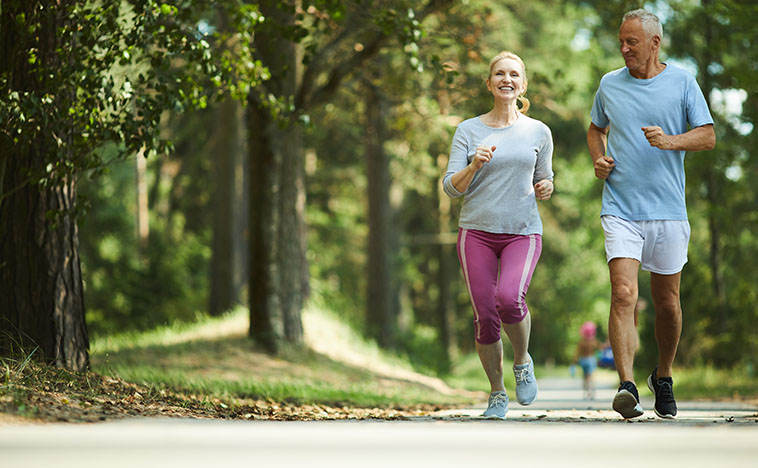 Active and healthy aged couple running in natural environment on summer morning