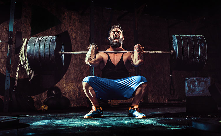 Muscular bearded tattoed fitness man doing deadlift a barbell over his head in modern fitness center. Functional training. Snatch exercise