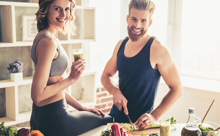 Beautiful young sports people are talking and smiling while cooking healthy food in kitchen at home